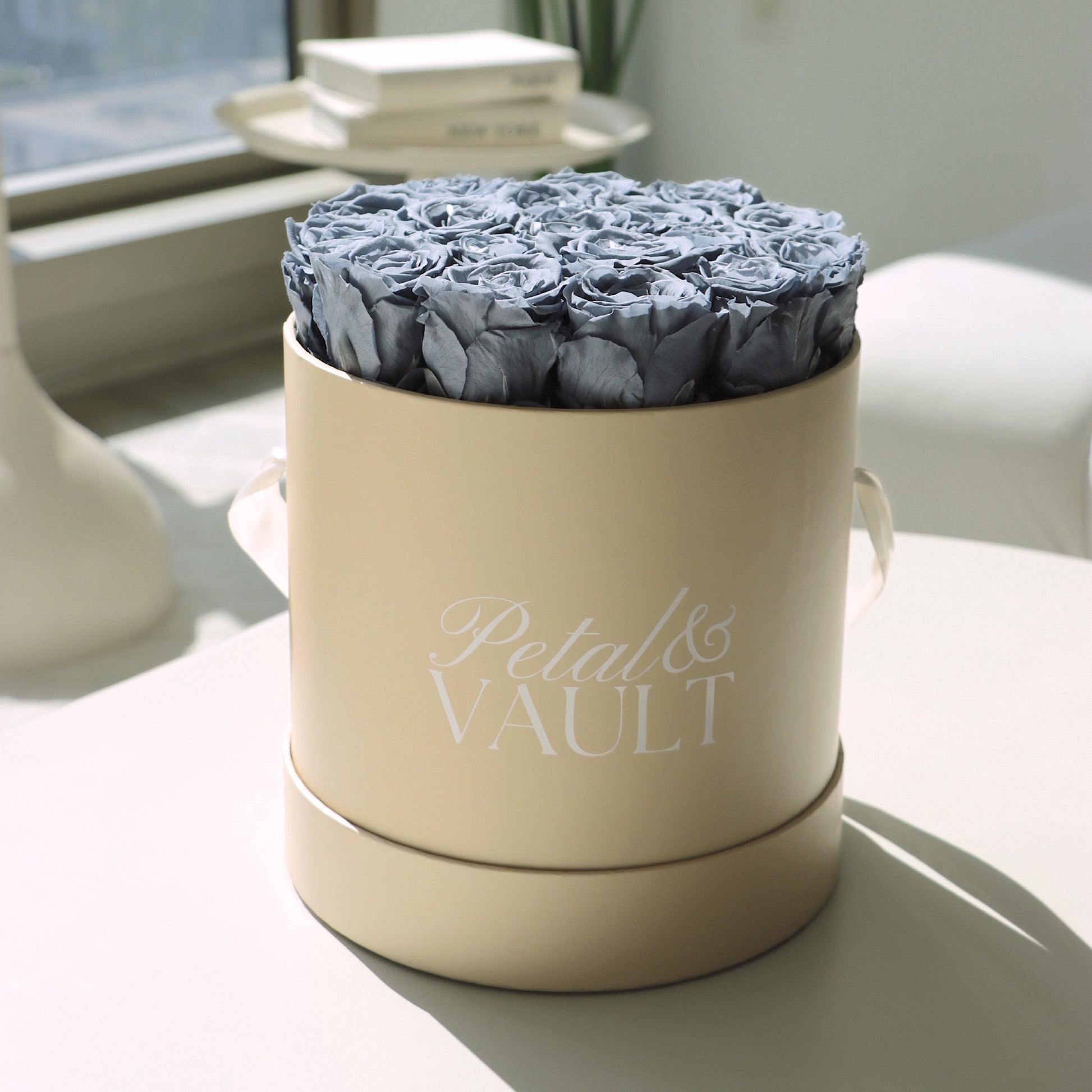 Beige round hat box with blue roses labeled 'Petal & Vault' on a light surface.