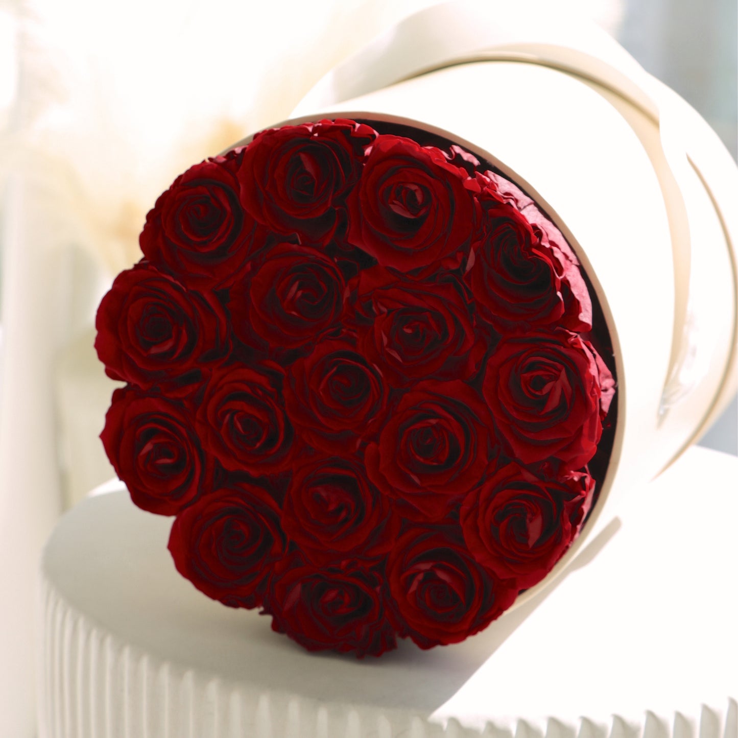 Round beige hat box container filled with vibrant preserved red roses on a white surface