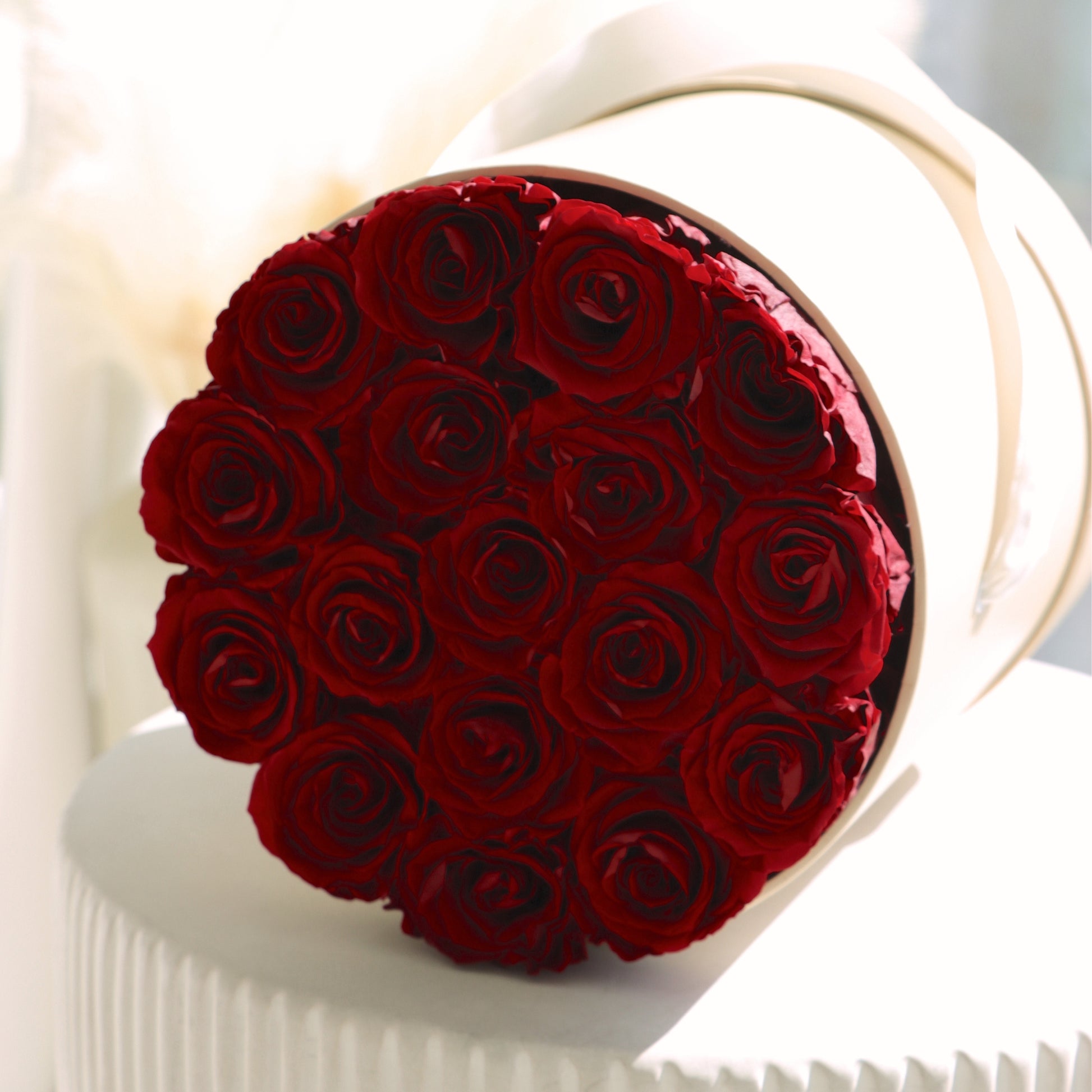 Round beige hat box container filled with vibrant preserved red roses on a white surface