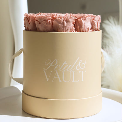 Beige cylindrical hat box with 'Petal & Vault' branding containing pink roses on a light mirrored background.